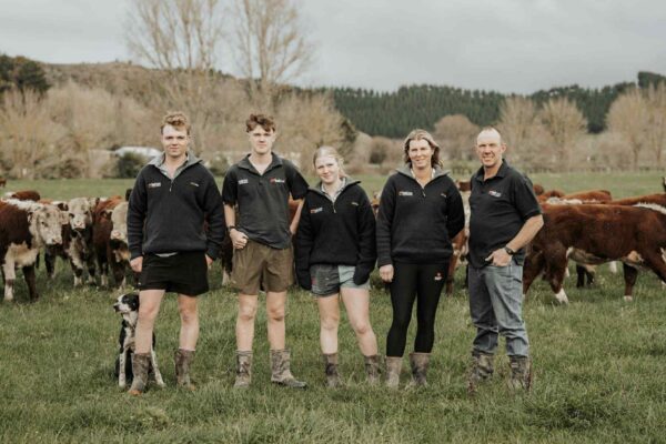 The Cranstone family of Riverton Ezicalve Herefords standing together on their Whanganui farm with their Hereford cattle in the background.