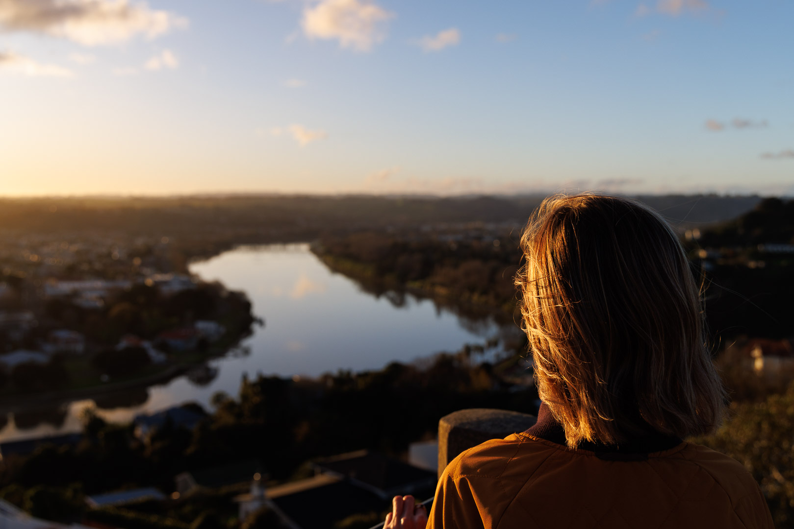 A person stands overlooking the Whanganui River at sunset, the light catching their hair. The view stretches out across the landscape, symbolising connection, care, and the community Hospice Whanganui serves.