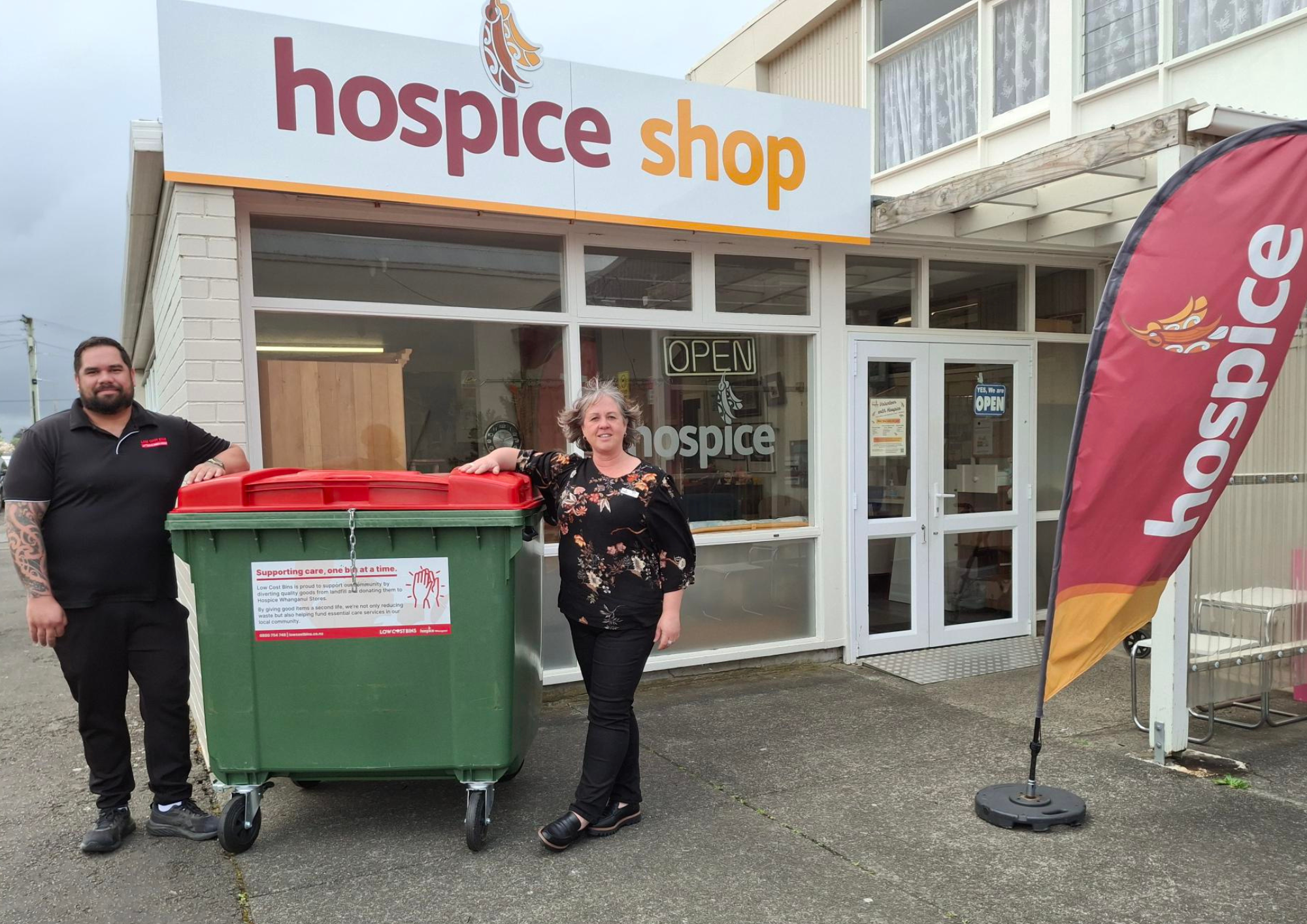 Jamie Houia from Low Cost Bins and Fiona McKinnon from Hospice Whanganui standing beside a donated refuse bin outside the Hospice Shop in Whanganui East.
