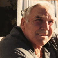 Portrait of Graham Dixon, an older man with white hair, sitting outdoors in the sunlight and looking to the side with a gentle smile.