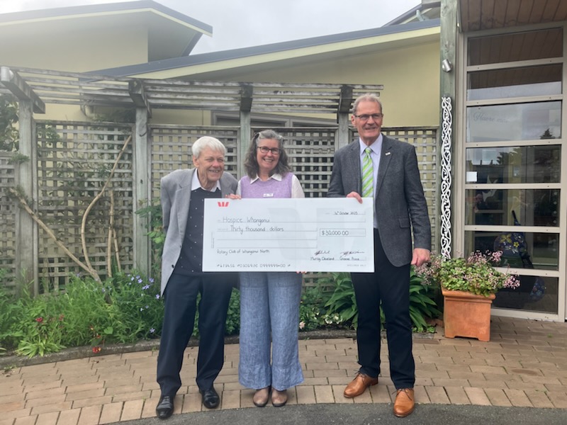 Representatives from Rotary Club of Whanganui North present a $30,000 donation cheque to Hospice Whanganui outside the hospice building. Three people stand smiling together, holding the large cheque.