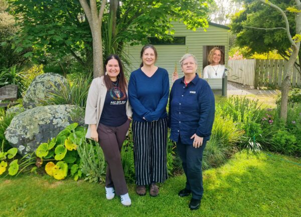 The Hospice Whanganui Whānau Support Team — Sam, Melissa, Carla, and Nelda (inset) — smiling together in the hospice gardens. The team stands among trees and greenery, representing the warmth, compassion, and collaboration they bring to supporting patients and their whānau.
