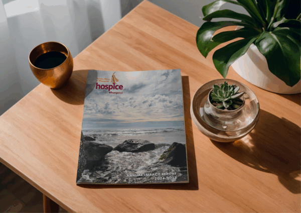 Hospice Whanganui 2024–25 Annual Impact Report resting on a wooden table beside a cup of coffee and a small potted succulent.