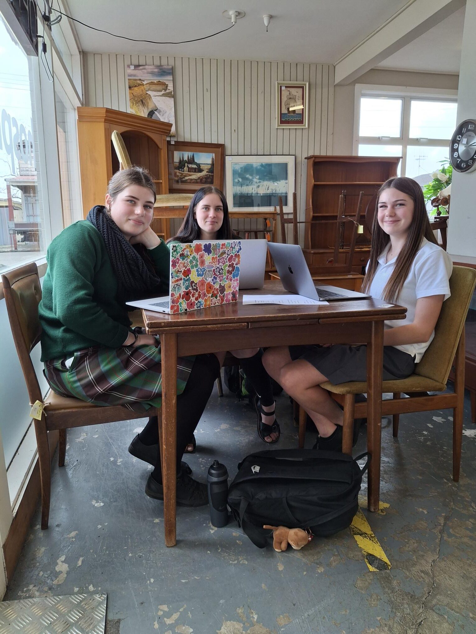 Whanganui High School students working on laptops inside a Hospice Whanganui shop, analysing customer survey responses.