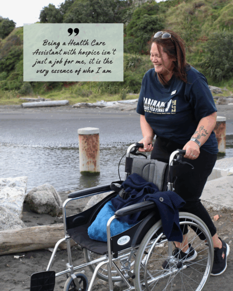 Hospice Whanganui Health Care Assistant Whina Broughton supporting a wheelchair outdoors, smiling and demonstrating compassionate care.