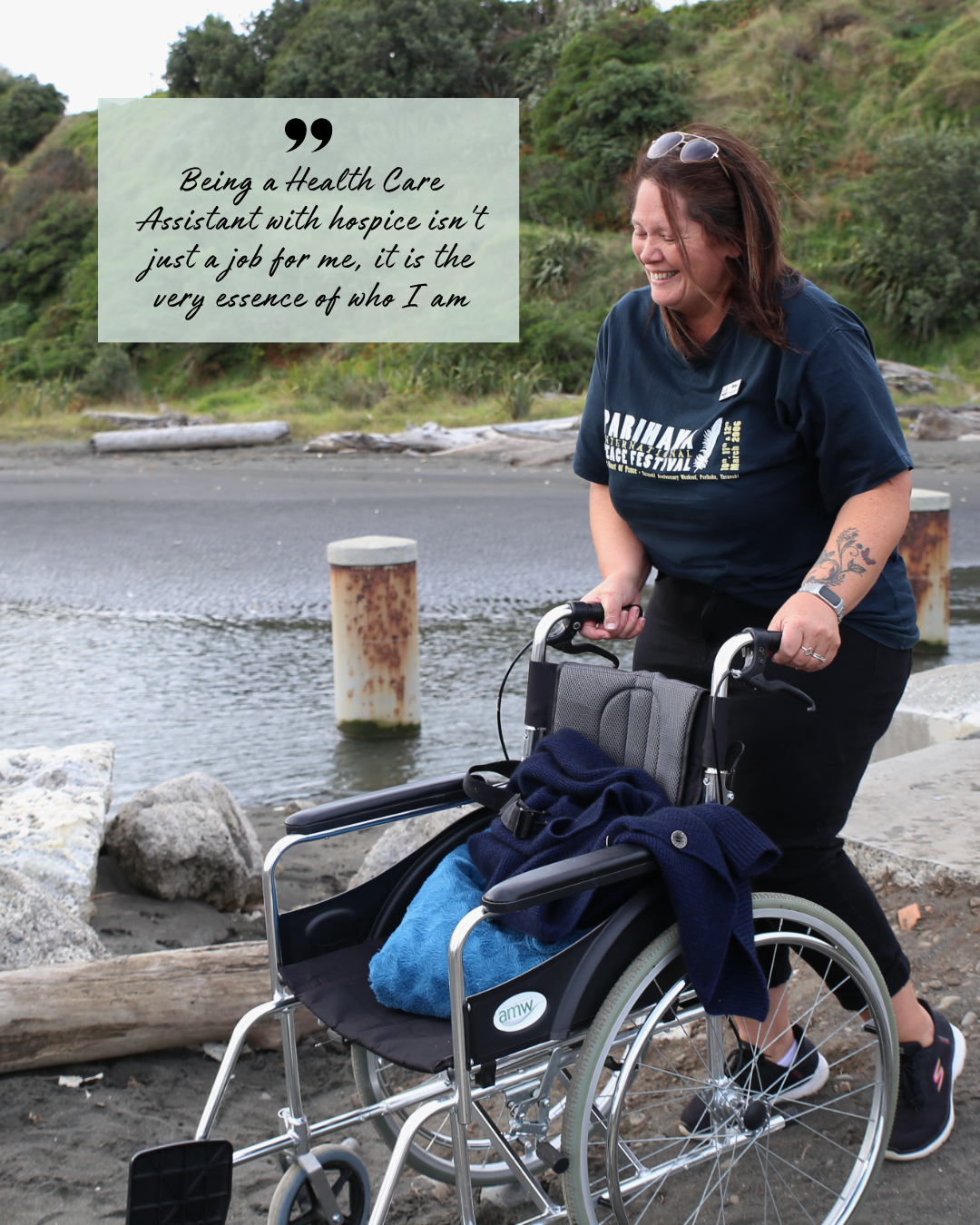 Hospice Whanganui Health Care Assistant Whina Broughton supporting a wheelchair outdoors, smiling and demonstrating compassionate care.